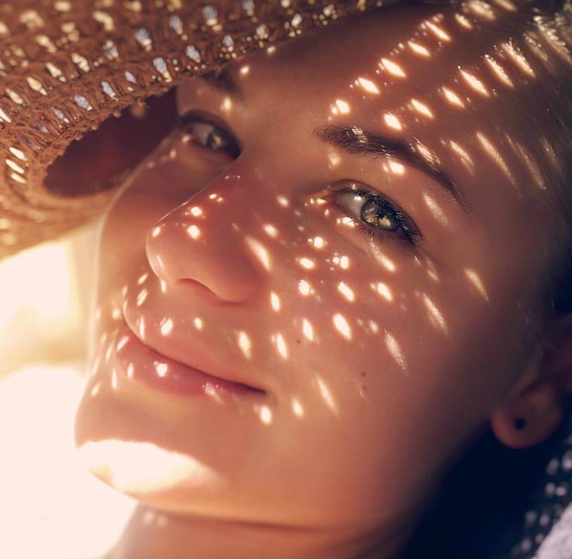 Closeup of smiling young woman holding a hat to shield brilliant sunshine