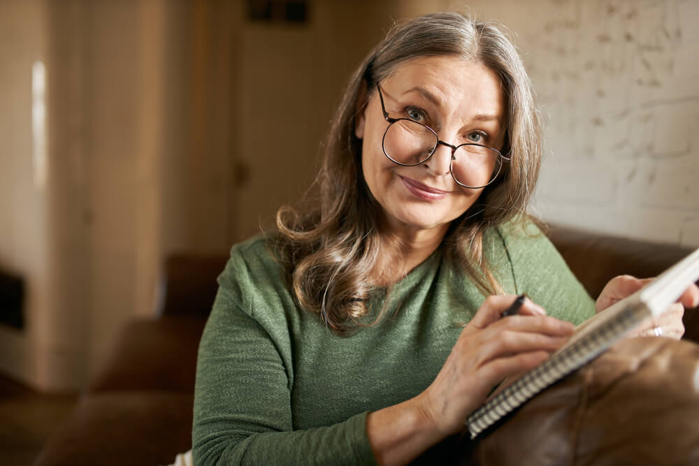 Older woman with large reading glasses writing in a notebook