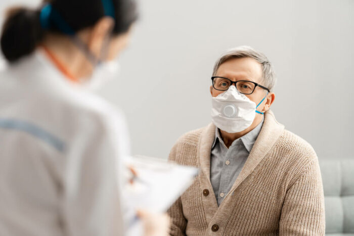 Man wearing a mask at a doctors office with a female doctor in the foreground