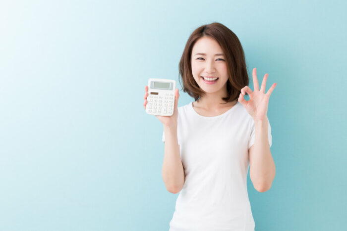 Smiling young holding a calculator. Light green backgound.